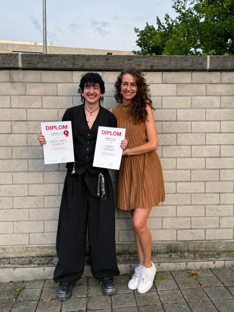 Two employees smiling, holding degree